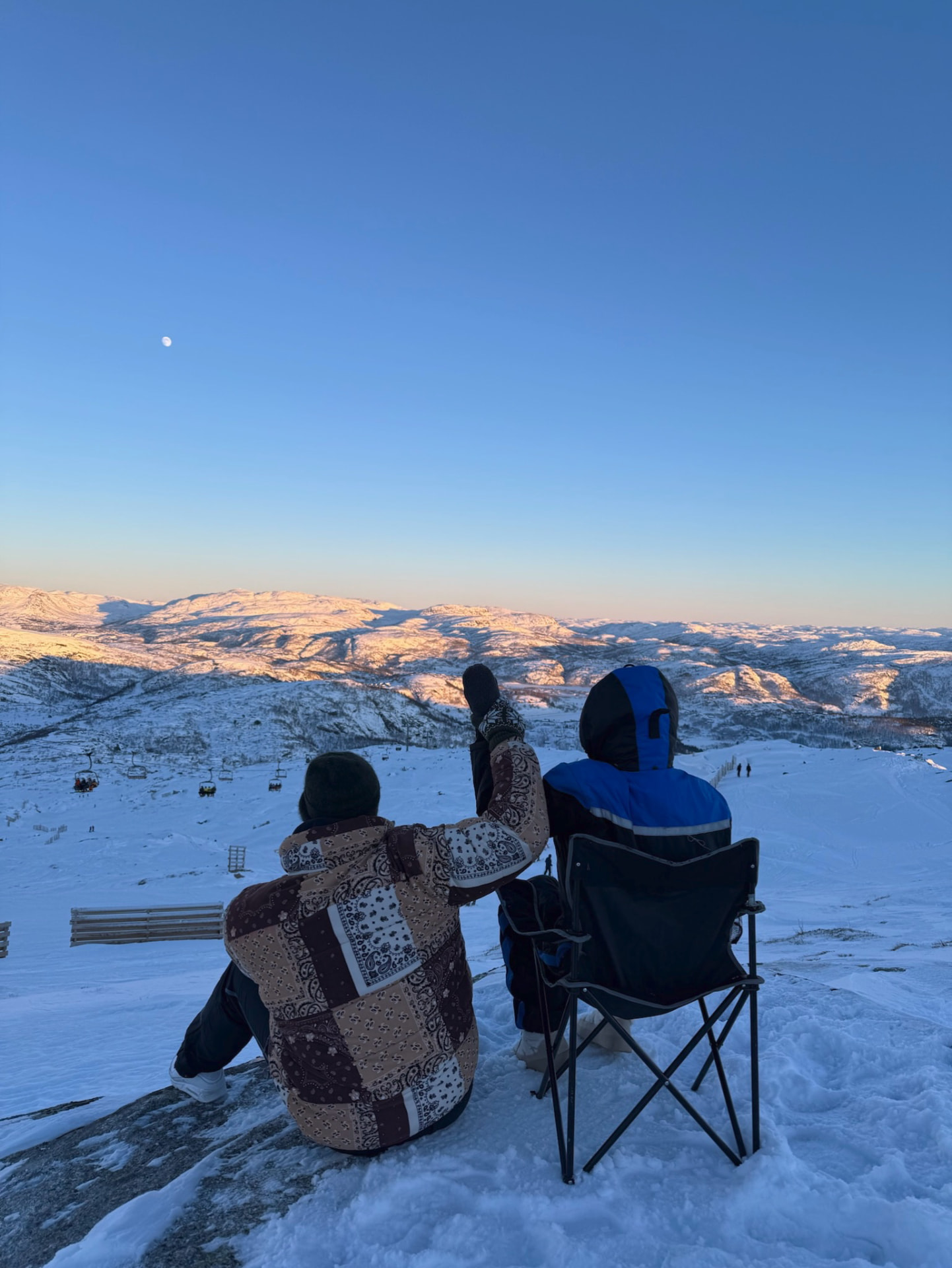 To personer sitter og ser ut over et snøkledt fjelllandskap