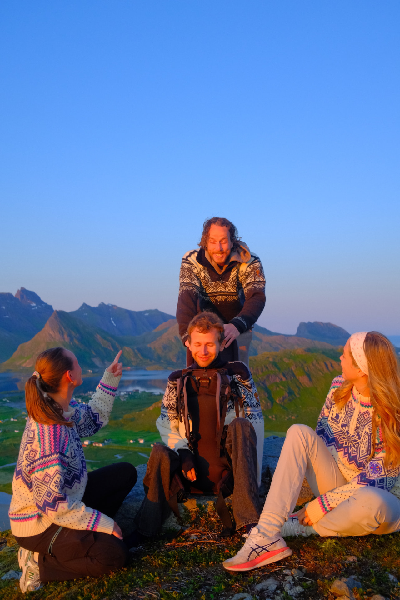 Gjengen samlet på en fjelltopp i kveldslys, med fjorder og tinder bak